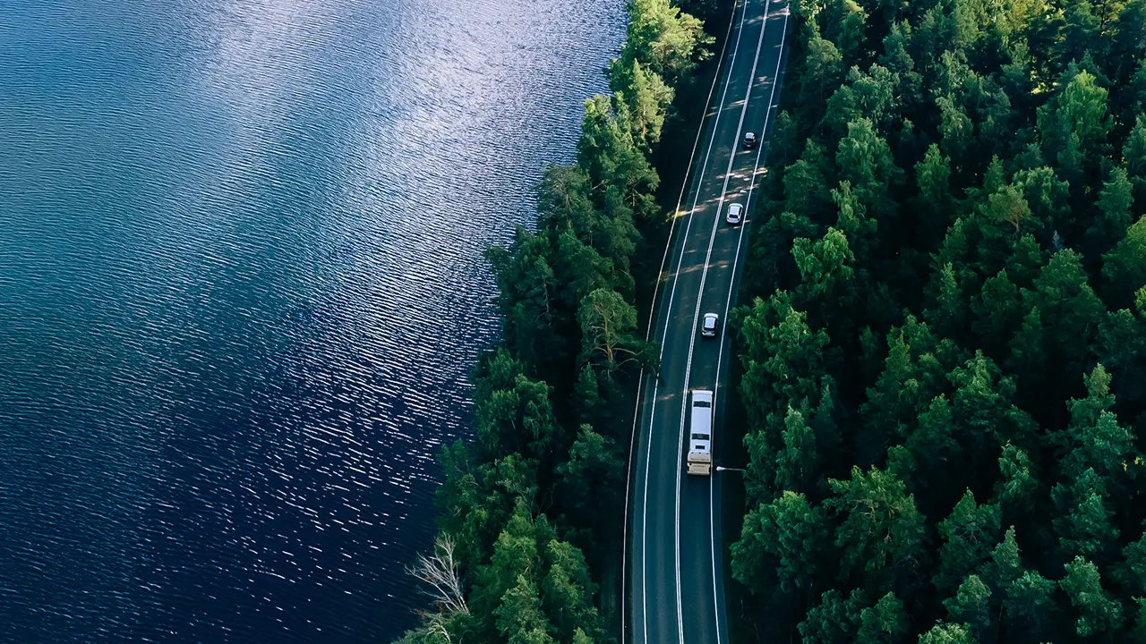 Bild tagen ovanifrån med en sjö till vänster och en bilväg med bilar till höger.
